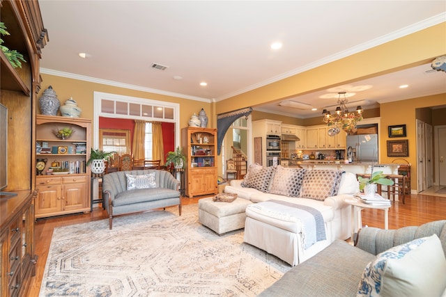 living room with light hardwood / wood-style floors, crown molding, and a notable chandelier