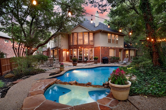 pool at dusk featuring grilling area, an in ground hot tub, and a patio