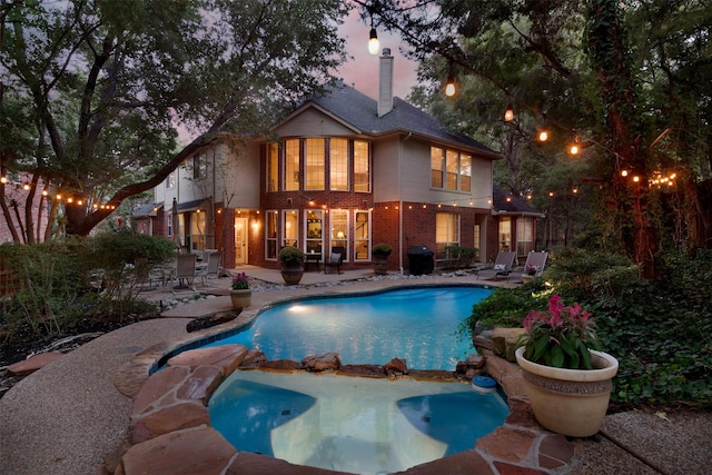 pool at dusk featuring a grill, a patio area, and an in ground hot tub