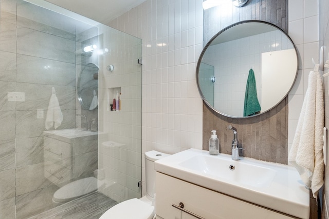 bathroom with toilet, tasteful backsplash, vanity, tile walls, and tiled shower