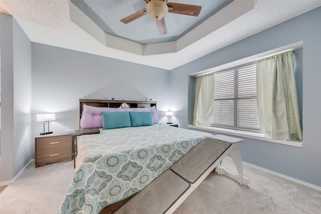 carpeted bedroom with ceiling fan, a textured ceiling, and a tray ceiling