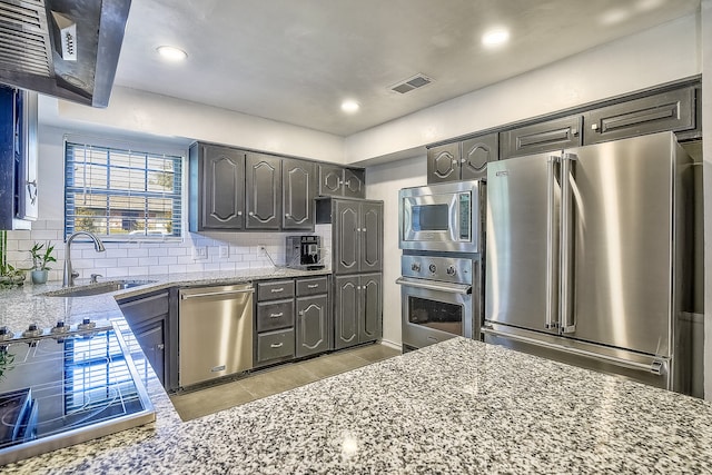 kitchen featuring light stone counters, sink, backsplash, and appliances with stainless steel finishes