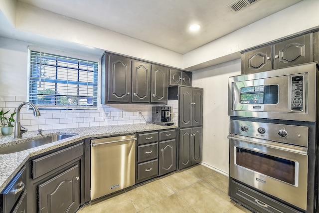 kitchen featuring light stone countertops, appliances with stainless steel finishes, light tile patterned floors, sink, and backsplash