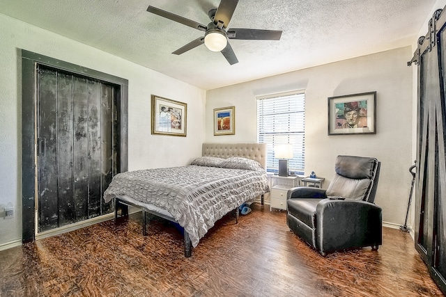 bedroom featuring a barn door, a textured ceiling, ceiling fan, and dark hardwood / wood-style flooring