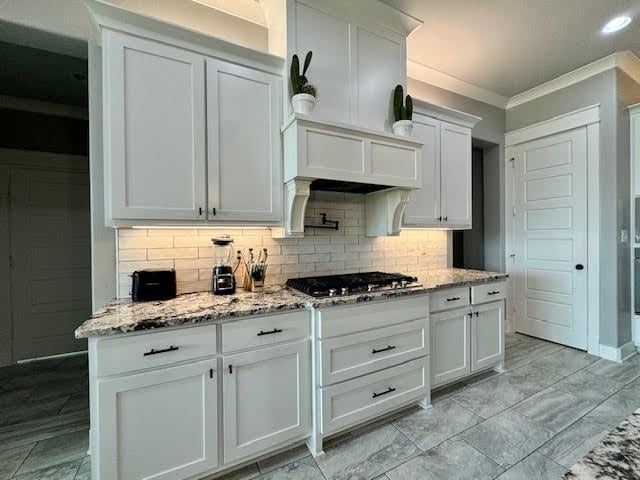 kitchen featuring light stone countertops, tasteful backsplash, crown molding, stainless steel gas cooktop, and white cabinetry