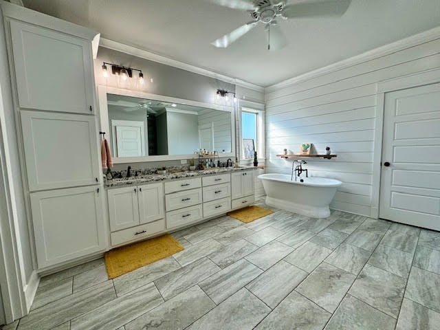 bathroom featuring ceiling fan, vanity, a bathtub, wooden walls, and crown molding