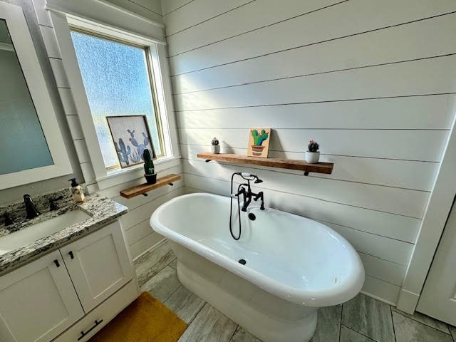 bathroom featuring a bathing tub, wood walls, and vanity