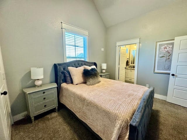 bedroom featuring dark colored carpet, ensuite bath, and vaulted ceiling