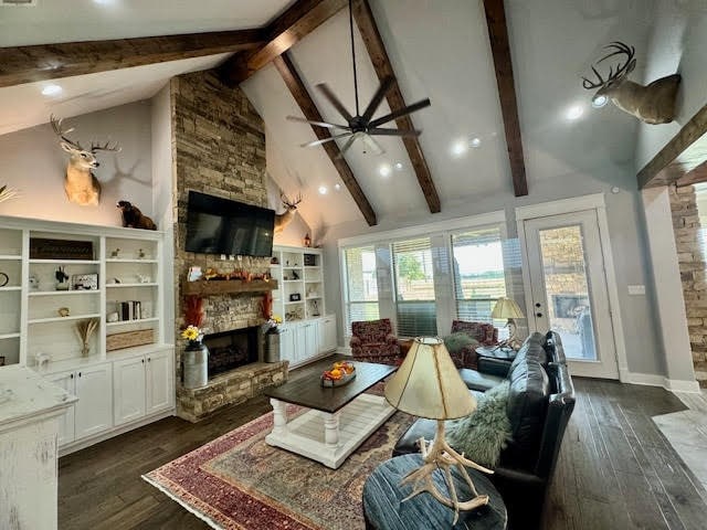 living room with ceiling fan, beam ceiling, a stone fireplace, and dark hardwood / wood-style flooring