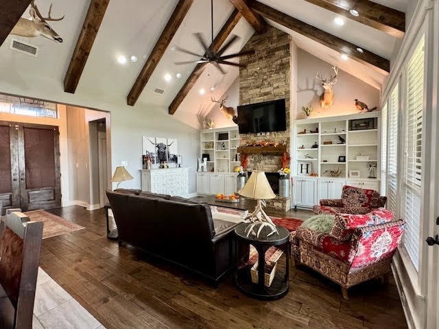 living room featuring beam ceiling, hardwood / wood-style flooring, and a stone fireplace