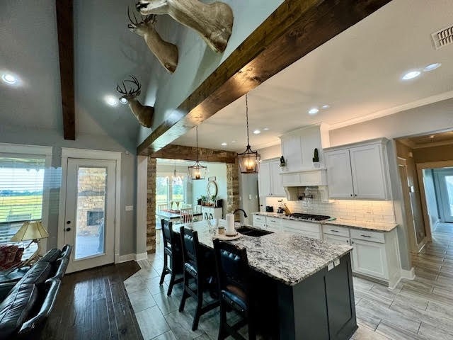 kitchen featuring light wood-type flooring, a kitchen island with sink, sink, white cabinetry, and beam ceiling