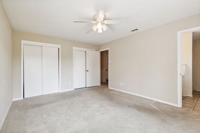 unfurnished bedroom featuring two closets, light carpet, and ceiling fan