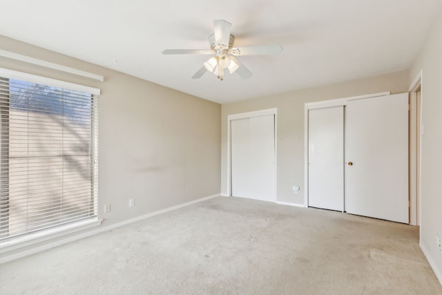 unfurnished bedroom featuring ceiling fan, multiple closets, and light carpet