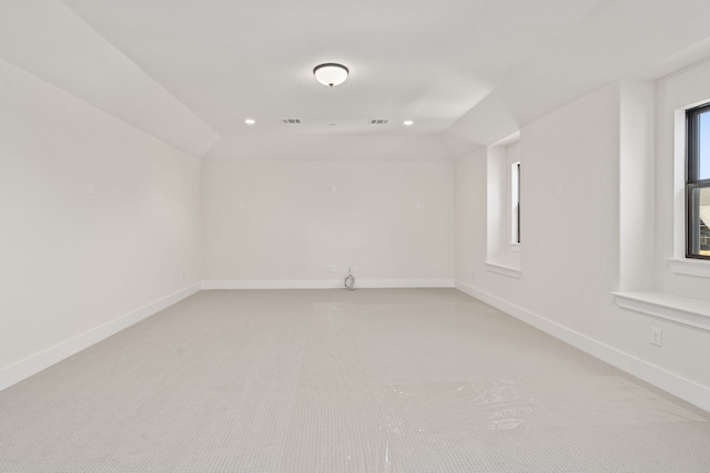 spare room with light colored carpet, visible vents, vaulted ceiling, and baseboards