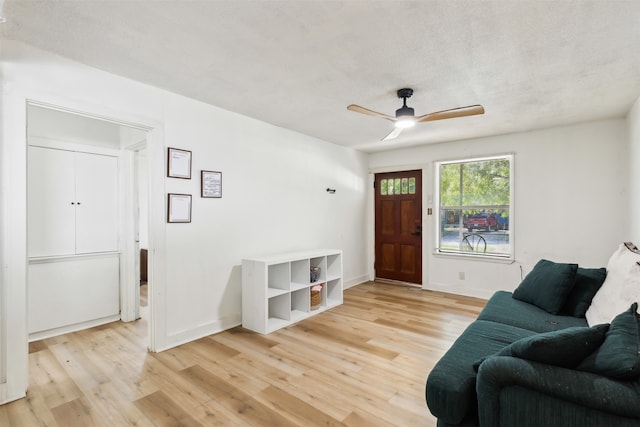 living room with light wood-type flooring, ceiling fan, and a textured ceiling