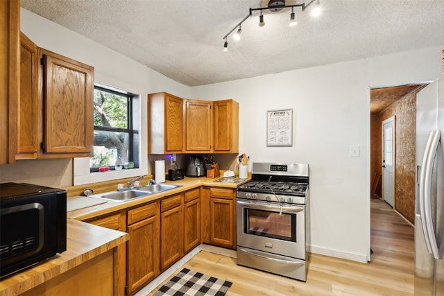 kitchen with light hardwood / wood-style floors, sink, a textured ceiling, stainless steel appliances, and track lighting