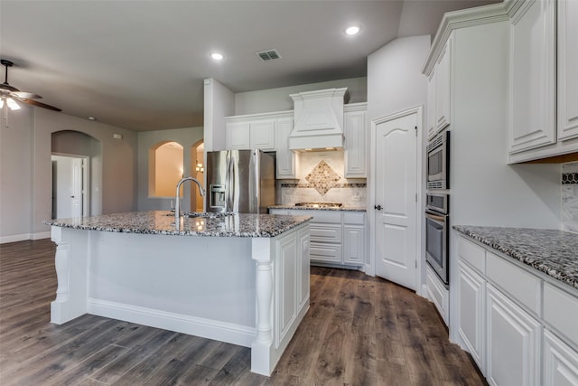 kitchen with premium range hood, an island with sink, white cabinets, dark stone counters, and stainless steel appliances