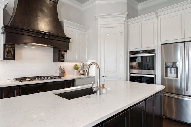 kitchen featuring custom exhaust hood, appliances with stainless steel finishes, ornamental molding, white cabinets, and tasteful backsplash