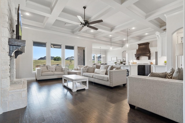 living room with a stone fireplace, ceiling fan, beamed ceiling, and dark hardwood / wood-style floors