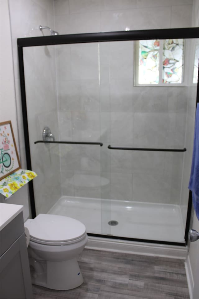 bathroom featuring hardwood / wood-style flooring, a shower with shower door, vanity, and toilet