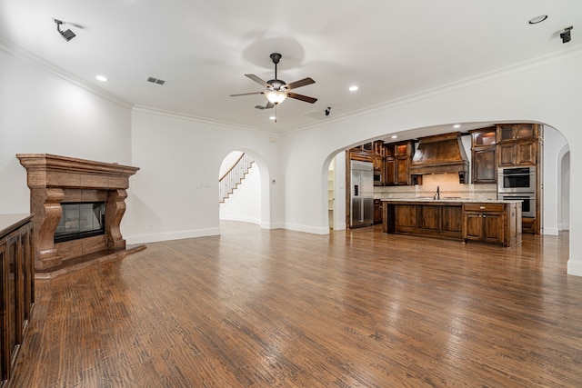 living room featuring sink, crown molding, dark wood-type flooring, a premium fireplace, and ceiling fan