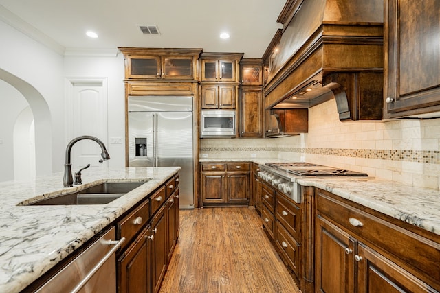 kitchen with dark wood-type flooring, sink, light stone counters, crown molding, and built in appliances