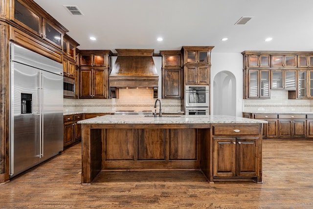 kitchen featuring a kitchen island with sink, sink, premium range hood, and appliances with stainless steel finishes