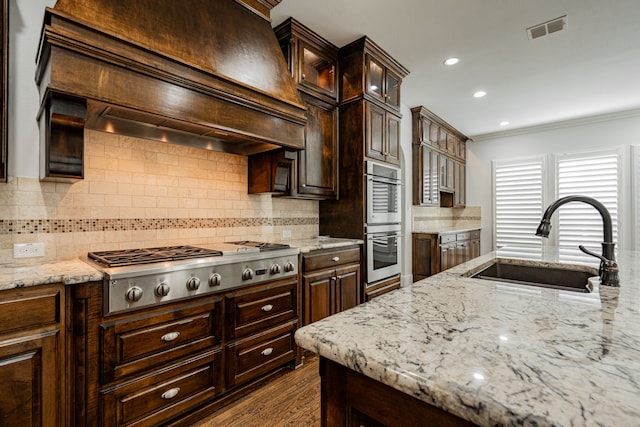 kitchen with premium range hood, dark brown cabinetry, sink, appliances with stainless steel finishes, and decorative backsplash