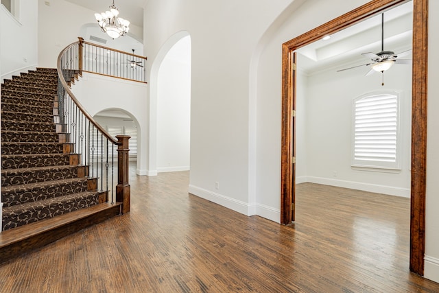 foyer entrance featuring ceiling fan with notable chandelier, dark wood-type flooring, and a high ceiling