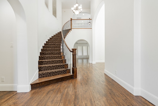 stairs with an inviting chandelier, a towering ceiling, and hardwood / wood-style floors