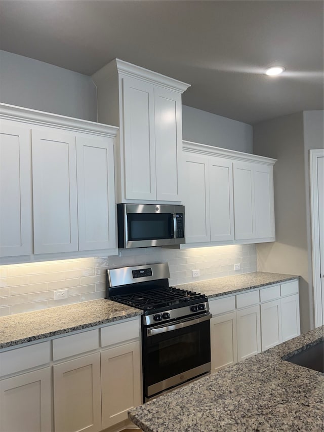 kitchen with light stone countertops, decorative backsplash, white cabinetry, and stainless steel appliances