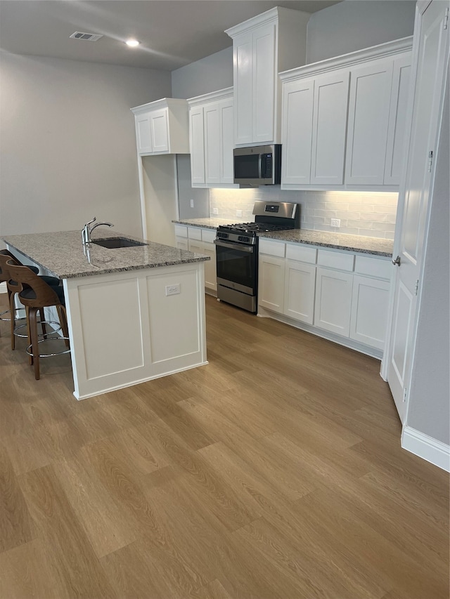 kitchen featuring sink, light wood-type flooring, an island with sink, white cabinetry, and stainless steel appliances