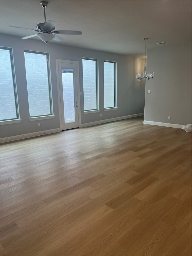 empty room featuring light hardwood / wood-style flooring, plenty of natural light, and ceiling fan with notable chandelier