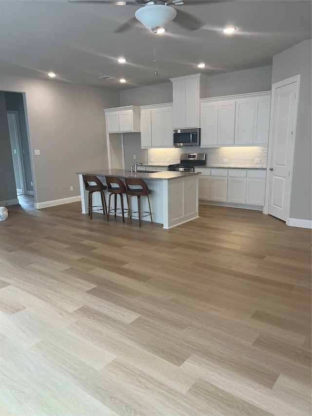 kitchen featuring a kitchen island with sink, a kitchen breakfast bar, stainless steel appliances, light wood-type flooring, and white cabinetry