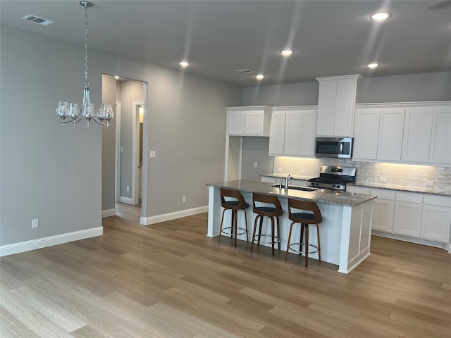 kitchen featuring an island with sink, light wood-type flooring, stainless steel appliances, stone countertops, and sink