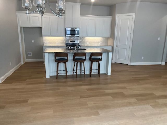 kitchen featuring a kitchen breakfast bar, stainless steel appliances, dark stone counters, white cabinets, and a center island with sink