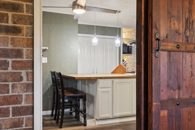 kitchen with pendant lighting, crown molding, a textured wall, wooden counters, and white cabinetry