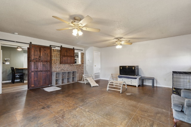 living area featuring a textured ceiling, a barn door, visible vents, a ceiling fan, and baseboards