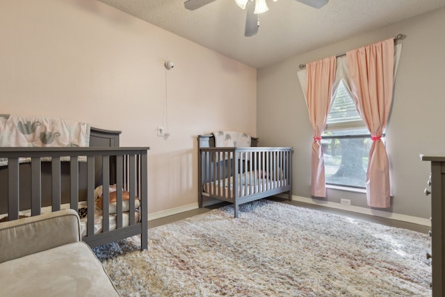 bedroom with a textured ceiling, a crib, a ceiling fan, and baseboards