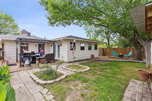 back of house with a chimney, a lawn, a patio area, fence, and a fire pit