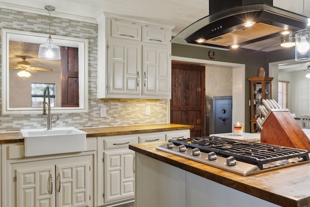 kitchen featuring island exhaust hood, stainless steel gas cooktop, butcher block counters, a ceiling fan, and a sink