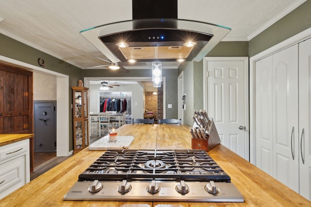 kitchen with island range hood, butcher block countertops, wood finished floors, ornamental molding, and stainless steel gas stovetop