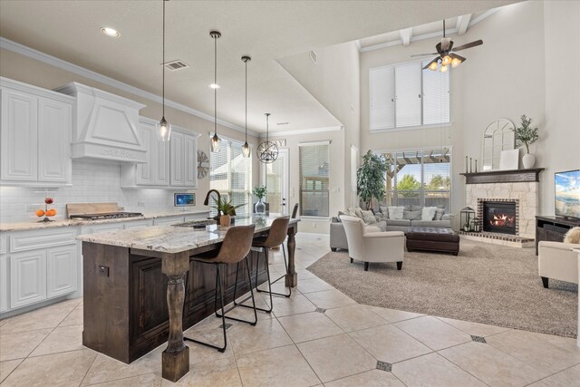 kitchen featuring custom exhaust hood, ceiling fan with notable chandelier, sink, light stone counters, and white cabinetry