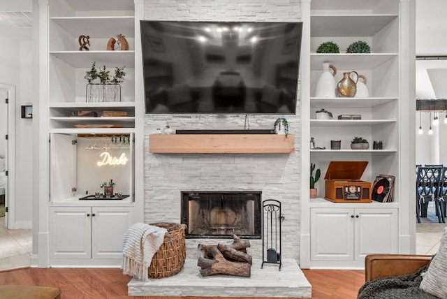 living room featuring built in shelves, light wood-type flooring, and a stone fireplace