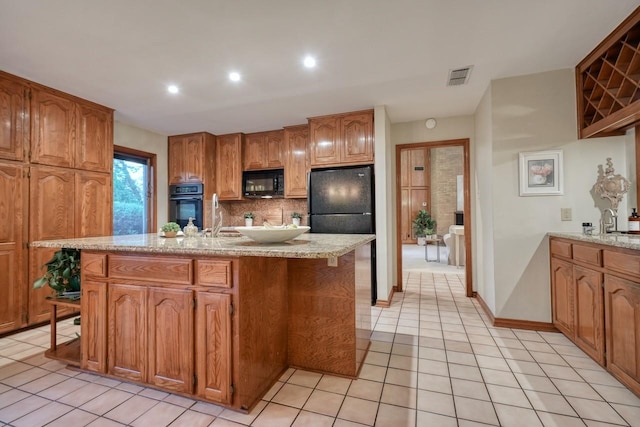 kitchen featuring sink, light stone counters, a kitchen island with sink, light tile patterned flooring, and black appliances