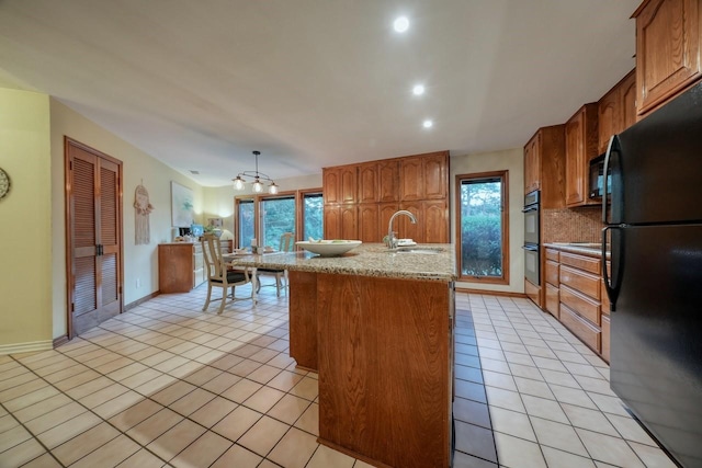 kitchen featuring pendant lighting, a kitchen island with sink, black appliances, sink, and light tile patterned flooring