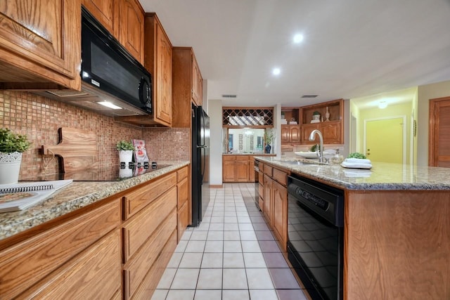 kitchen featuring sink, tasteful backsplash, a center island with sink, light tile patterned flooring, and black appliances