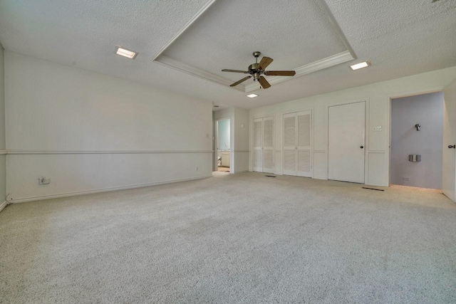 carpeted empty room featuring a textured ceiling, a raised ceiling, and ceiling fan