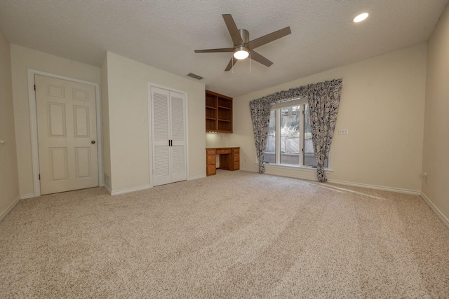 unfurnished bedroom with ceiling fan, built in desk, a textured ceiling, carpet floors, and a closet