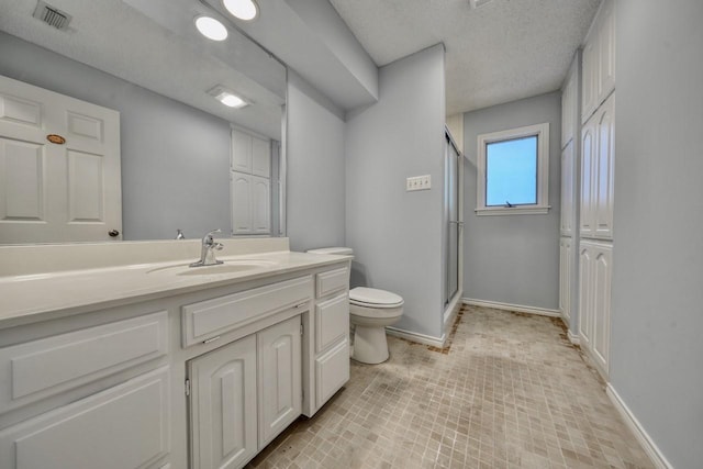 bathroom featuring vanity, toilet, a shower with door, and a textured ceiling